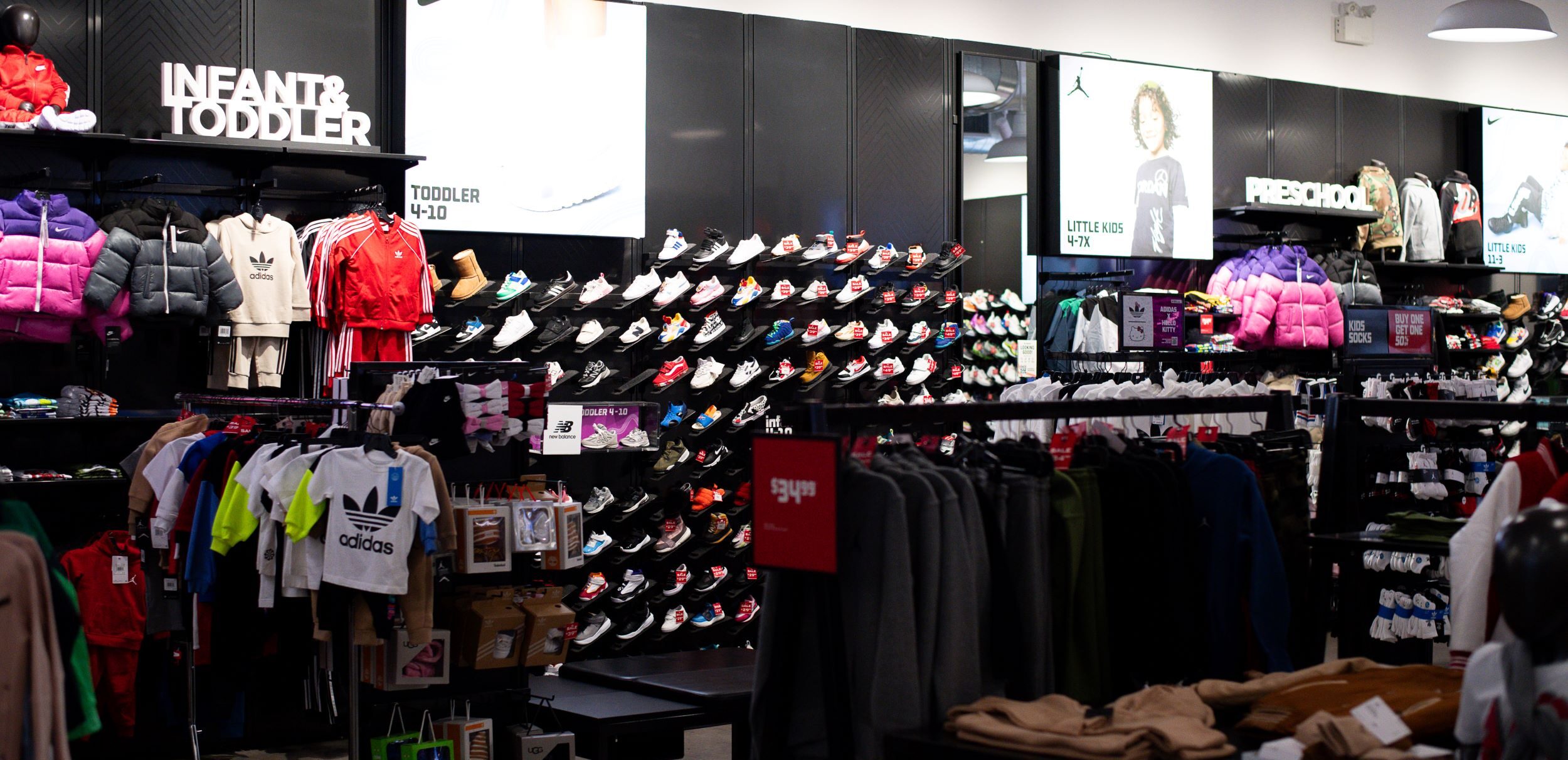 Interior of a sports apparel store featuring a range of products, including sneakers on shelves, toddler clothes, and various branded athletic wear.