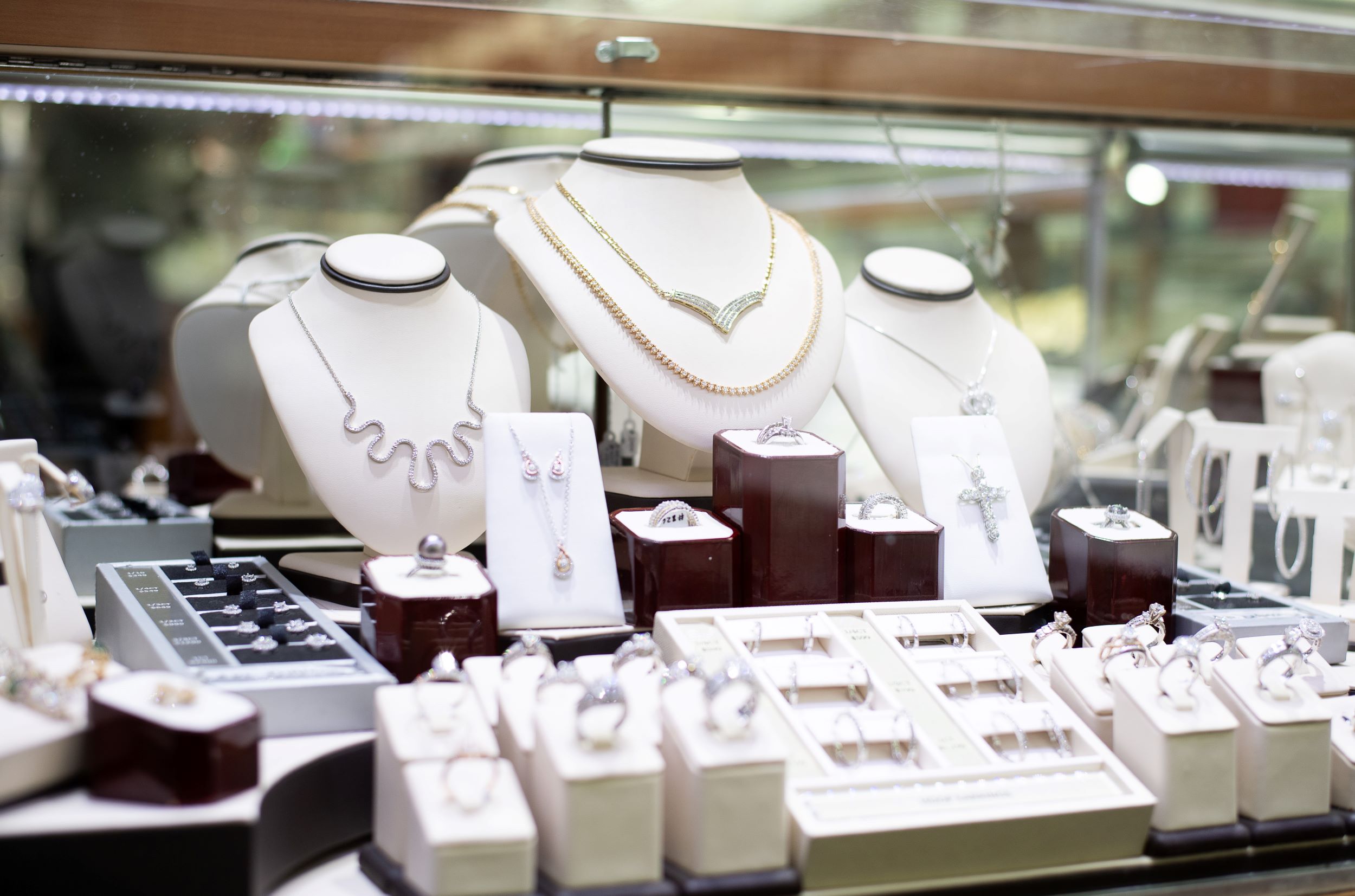 An array of elegant jewelry displayed on stands and in boxes inside a glass showcase, featuring necklaces, earrings, and rings in a store setting.