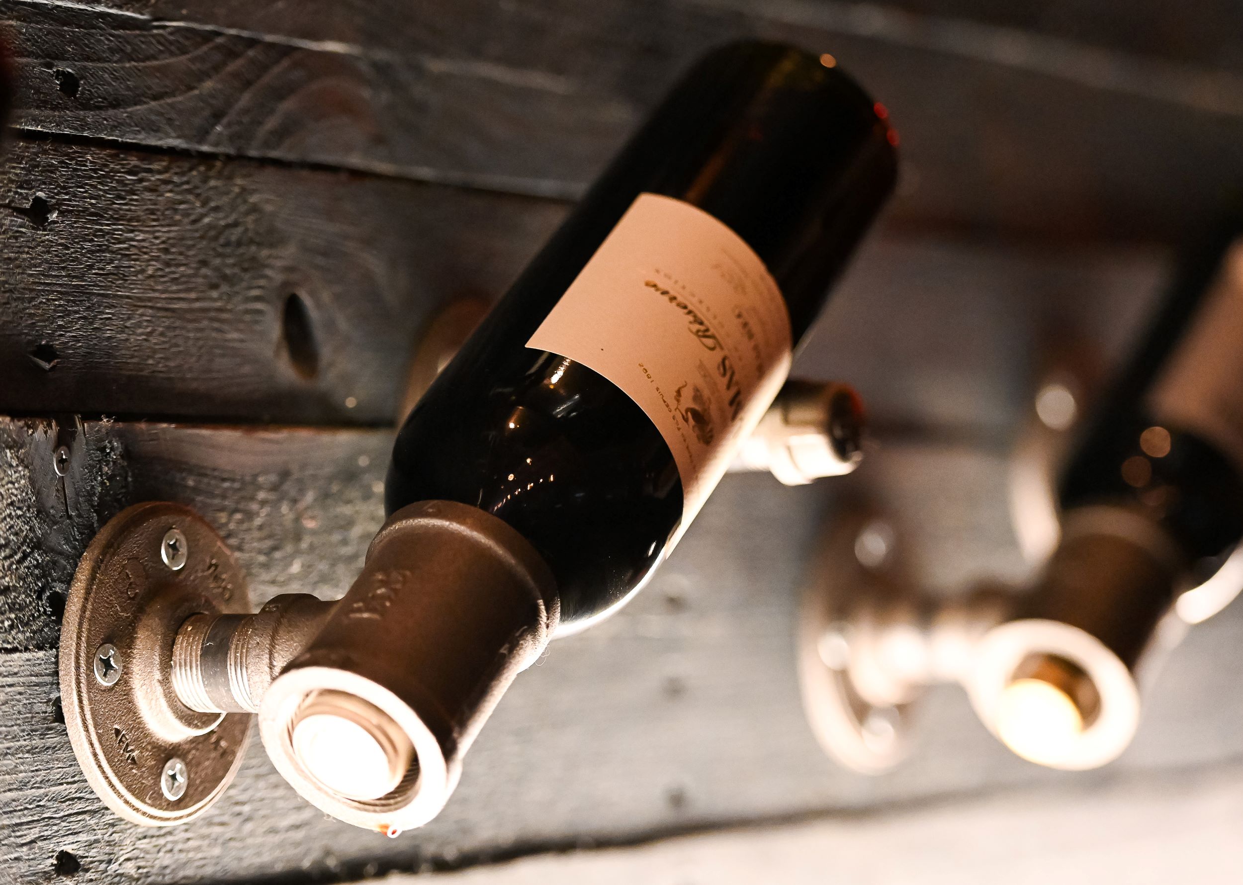 Bottles of wine horizontally mounted on a rustic wooden rack with metal brackets, focusing on one bottle in sharp detail.