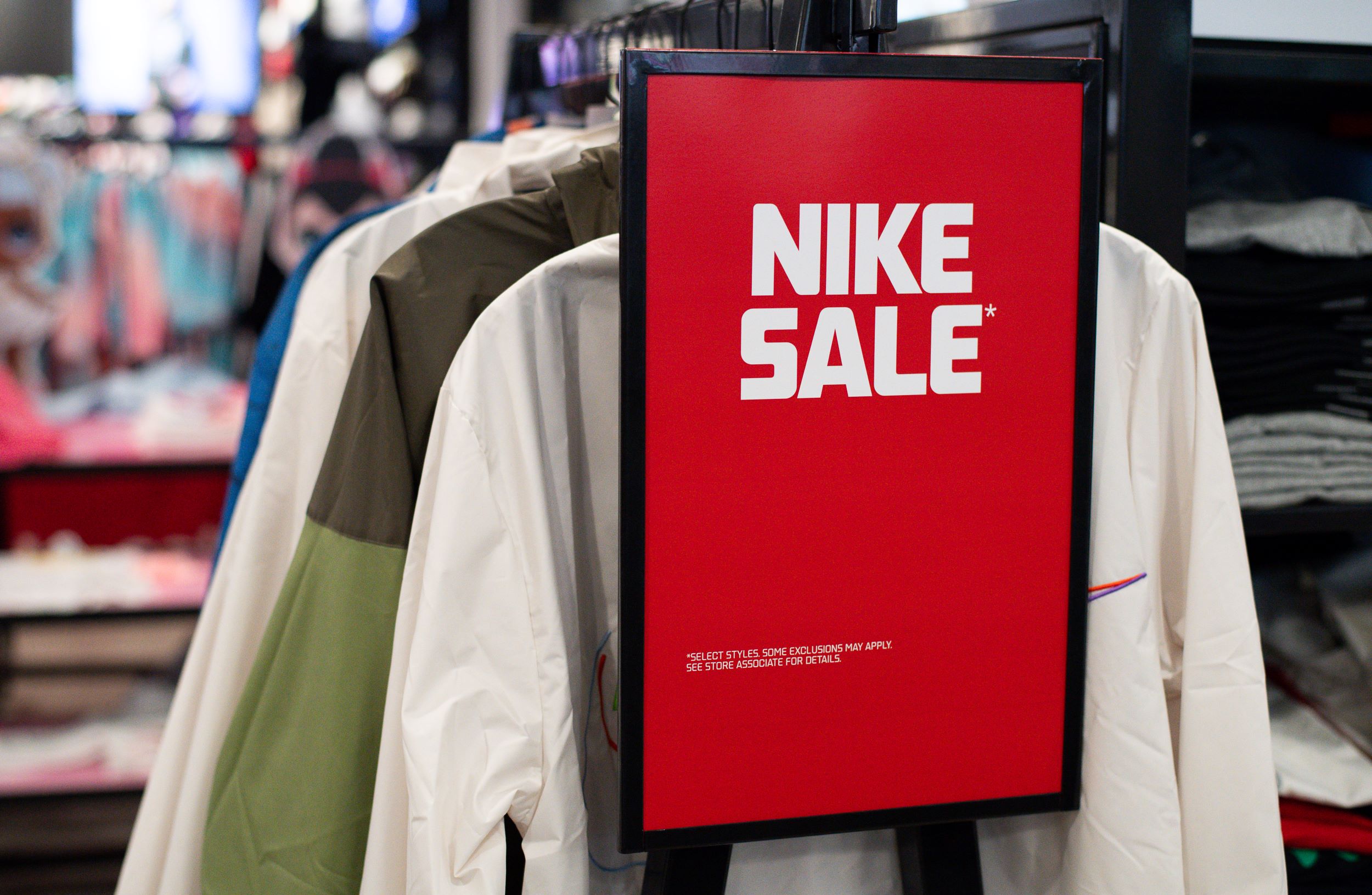 A red nike sale sign hanging in a clothing store surrounded by jackets on display.