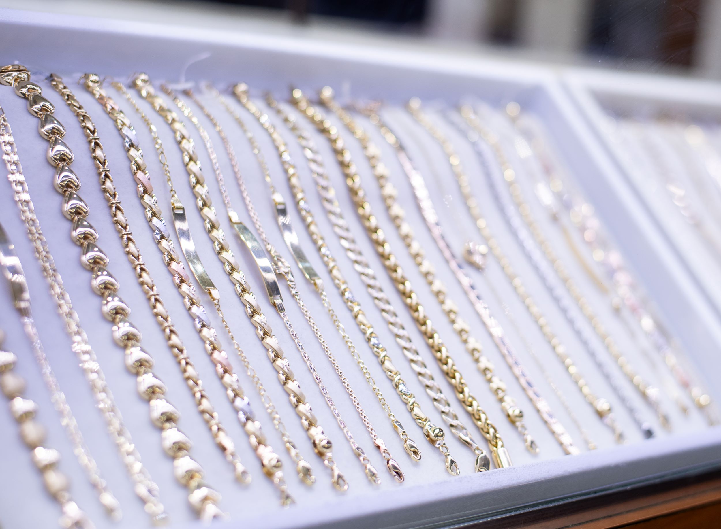 An array of gold and silver necklaces displayed neatly in a glass jewelry case, with varying designs and sizes, creating a shimmering effect.