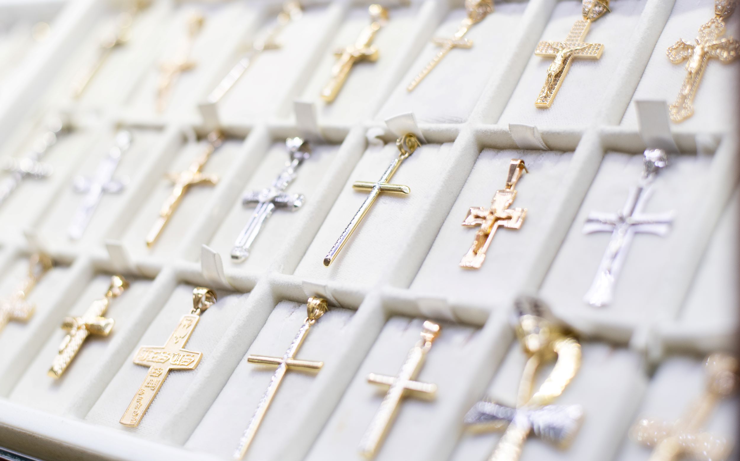 A selection of various cross pendants displayed in a jewelry store tray, featuring different designs and materials with a focus on a central gold cross.