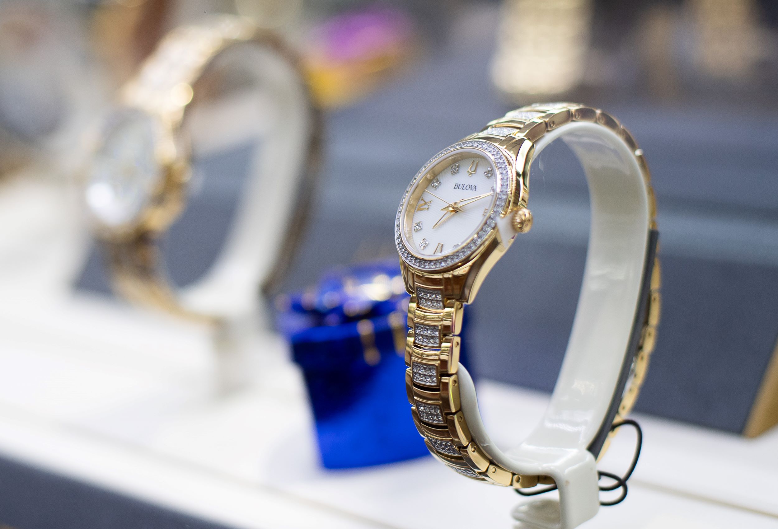 Two elegant wristwatches on display, one in the foreground focused with a golden band and white dial, and another slightly blurred in the background.