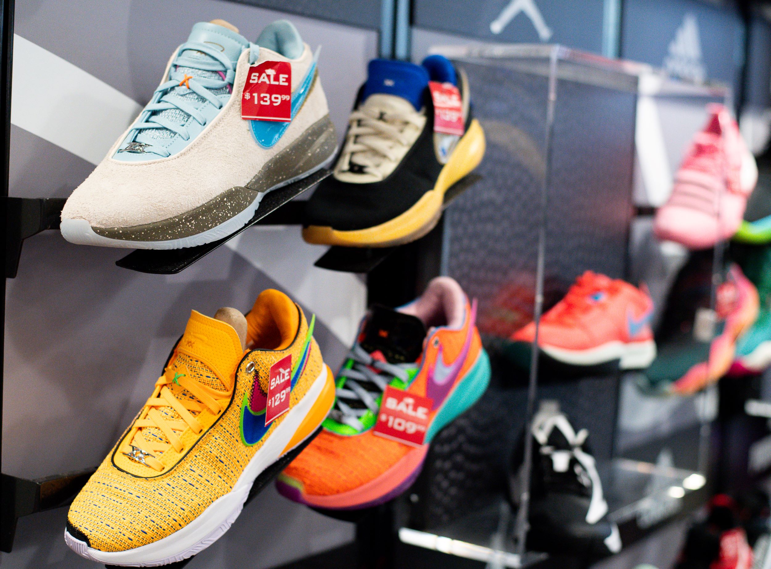 Colorful sneakers on display with sale tags, highlighting a variety of styles and brands on a shoe rack in a store.