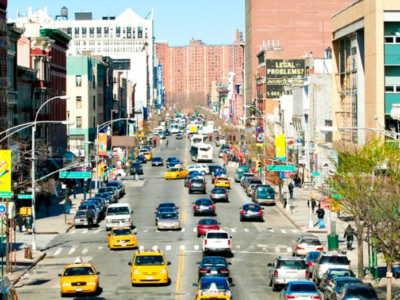 A bustling city street scene with rows of colorful cars and taxis, flanked by tall buildings under a blue sky. billboards and street signs add urban detail.