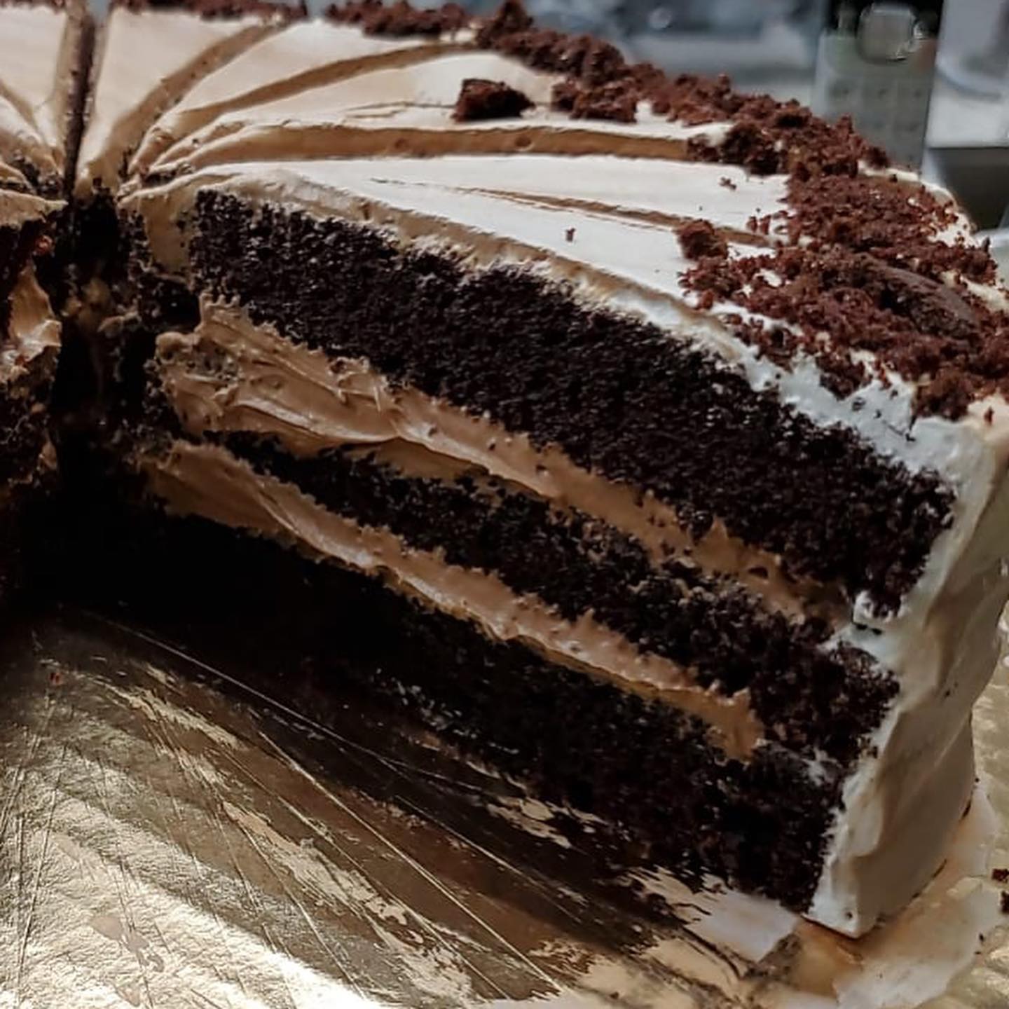 Close-up of a sliced chocolate cake with multiple layers of dark sponge and thick cream frosting, topped with crumbled chocolate.