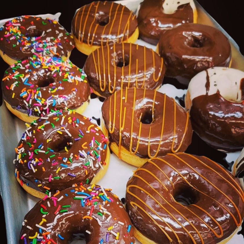 A tray filled with assorted donuts, some topped with rainbow sprinkles and others drizzled with chocolate and caramel icing.