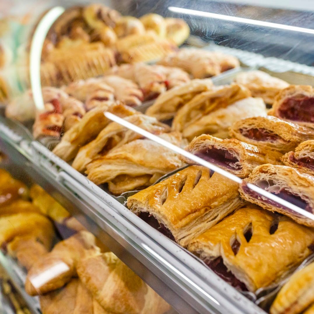A display case filled with various freshly baked pastries, including fruit-filled turnovers and puff pastries, each showing golden-brown crusts and visible fillings.