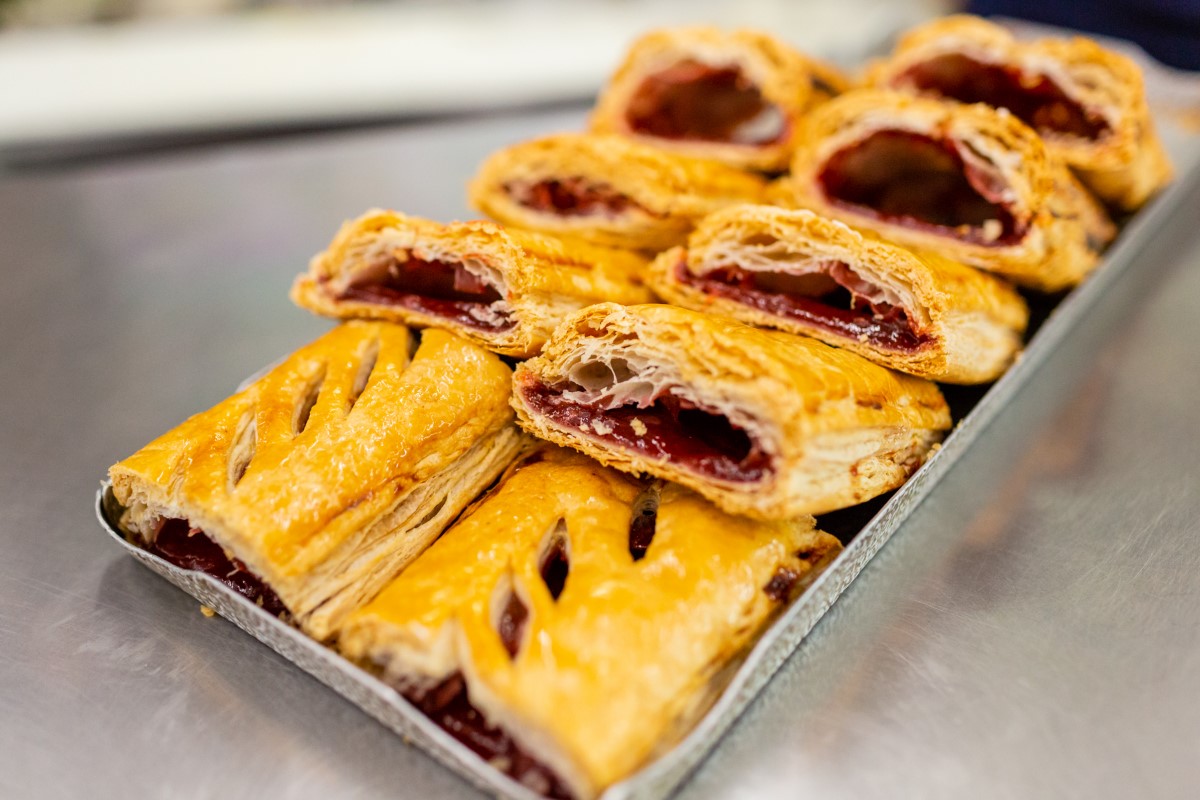 A tray of freshly baked cherry turnovers with flaky golden crusts, revealing vibrant red cherry filling, displayed on a kitchen counter.