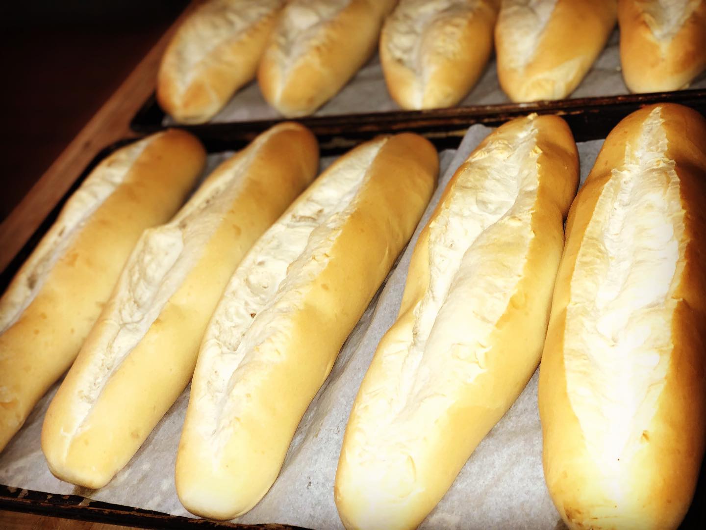 Freshly baked baguettes on a tray lined with parchment paper, showing a golden crust and soft texture.
