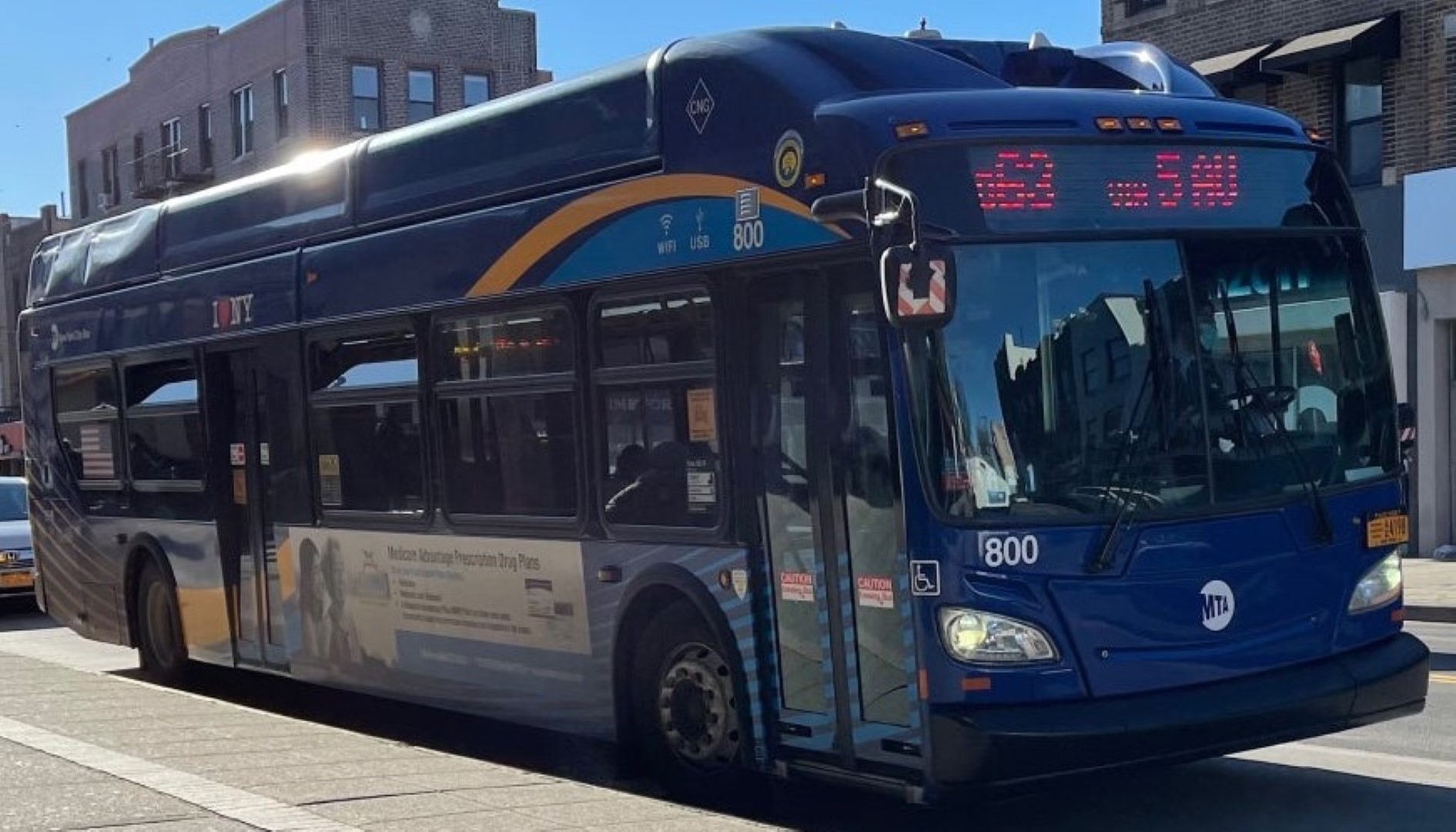 A blue mta bus is parked, displaying route "s79 sbs" on a sunny day. it features sleek modern design with a distinctive curvy roof and large front windows.
