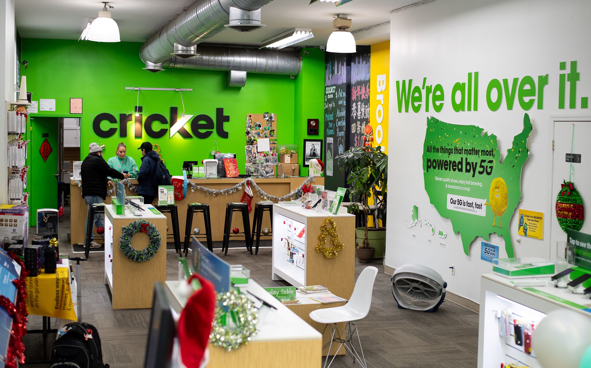 Interior of a cricket wireless store decorated with christmas ornaments. customers and employees interact near the service counters under bright lighting.