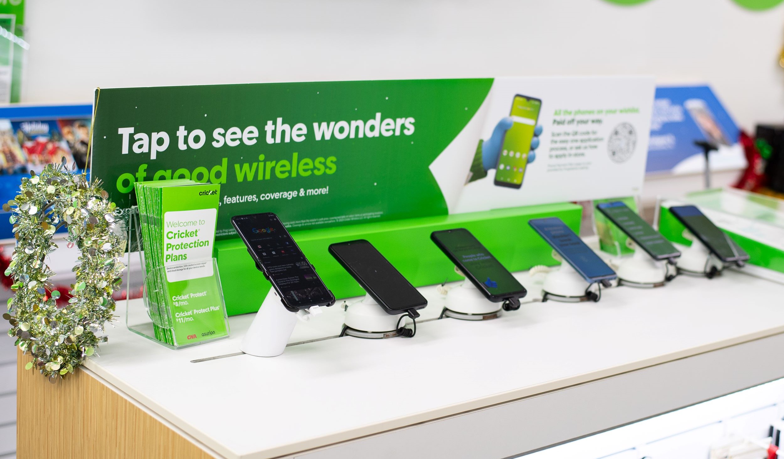 A display of various smartphones secured on a counter with a green promotional cricket wireless banner in the background at a store.