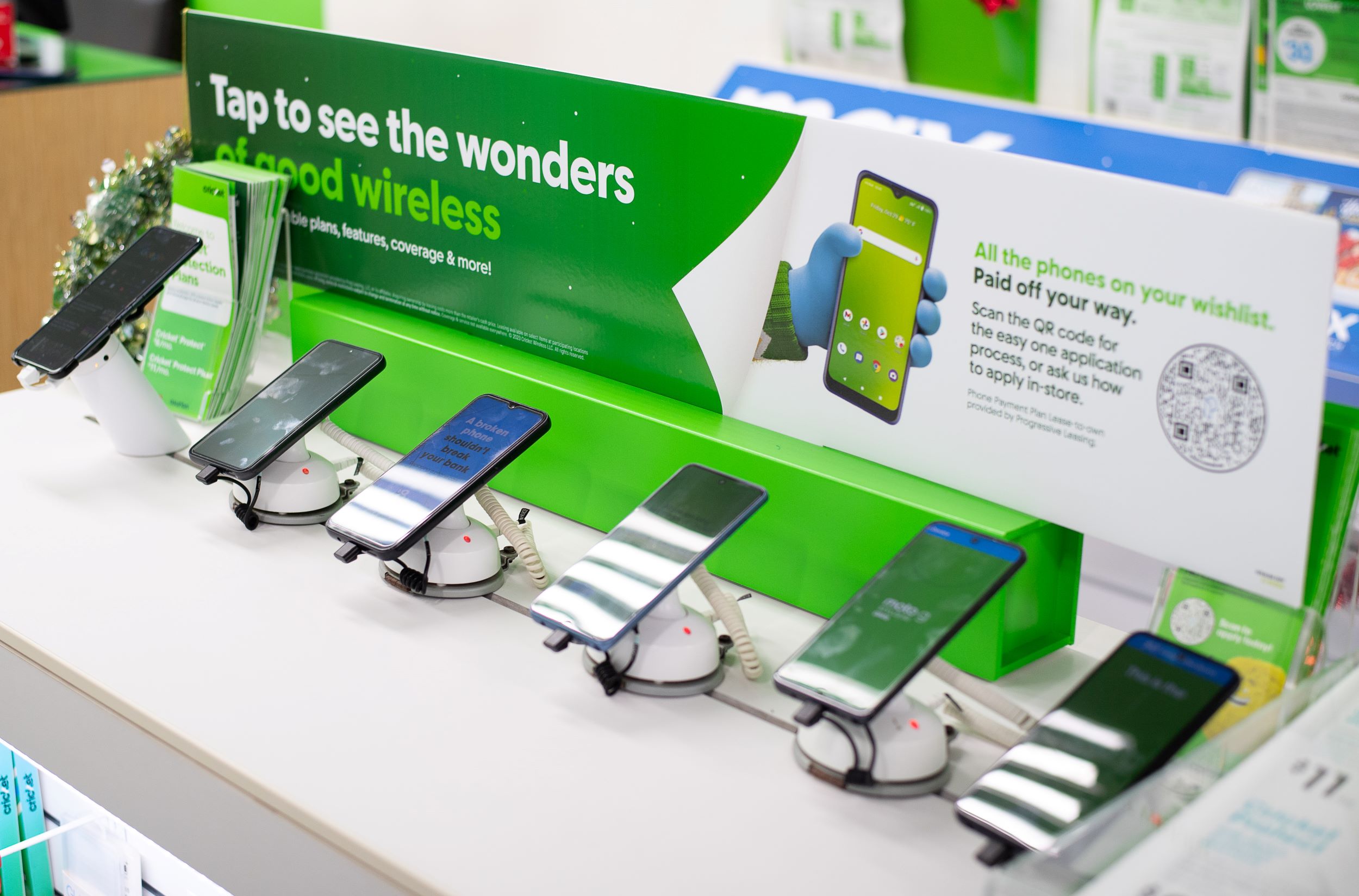 A display of smartphones on a store counter under signs promoting wireless services and special offers, with some green holiday decorations visible.