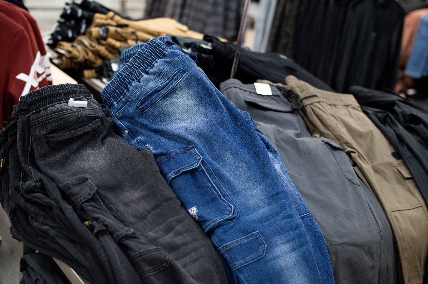 A variety of trousers displayed in a store, including blue jeans and several pairs in shades of gray and black. the focus is on the detailed textures of the fabrics.