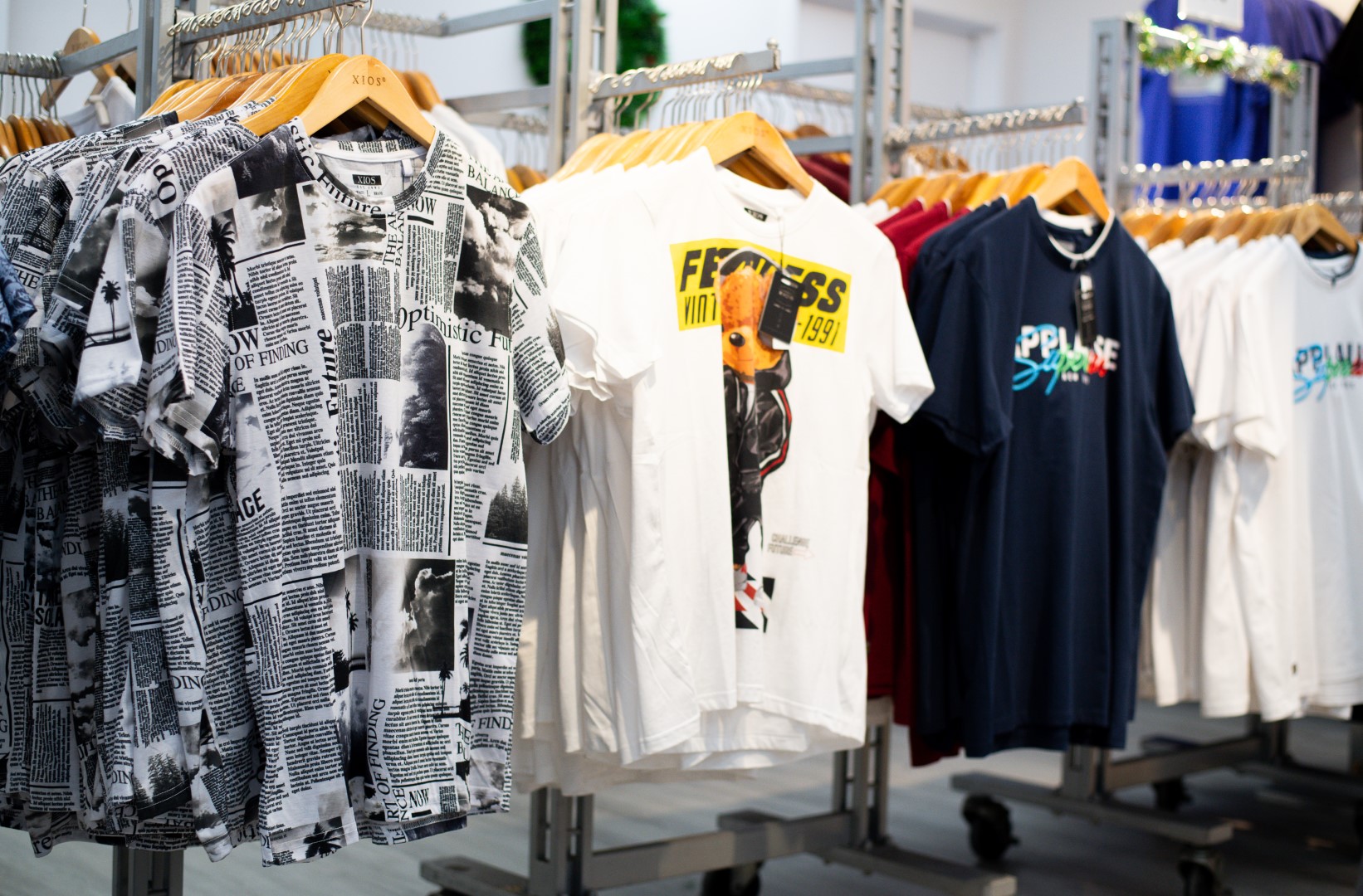 Colorful t-shirts with various prints hanging on display racks in a clothing store, including one with a newspaper design and another with bold graphics.