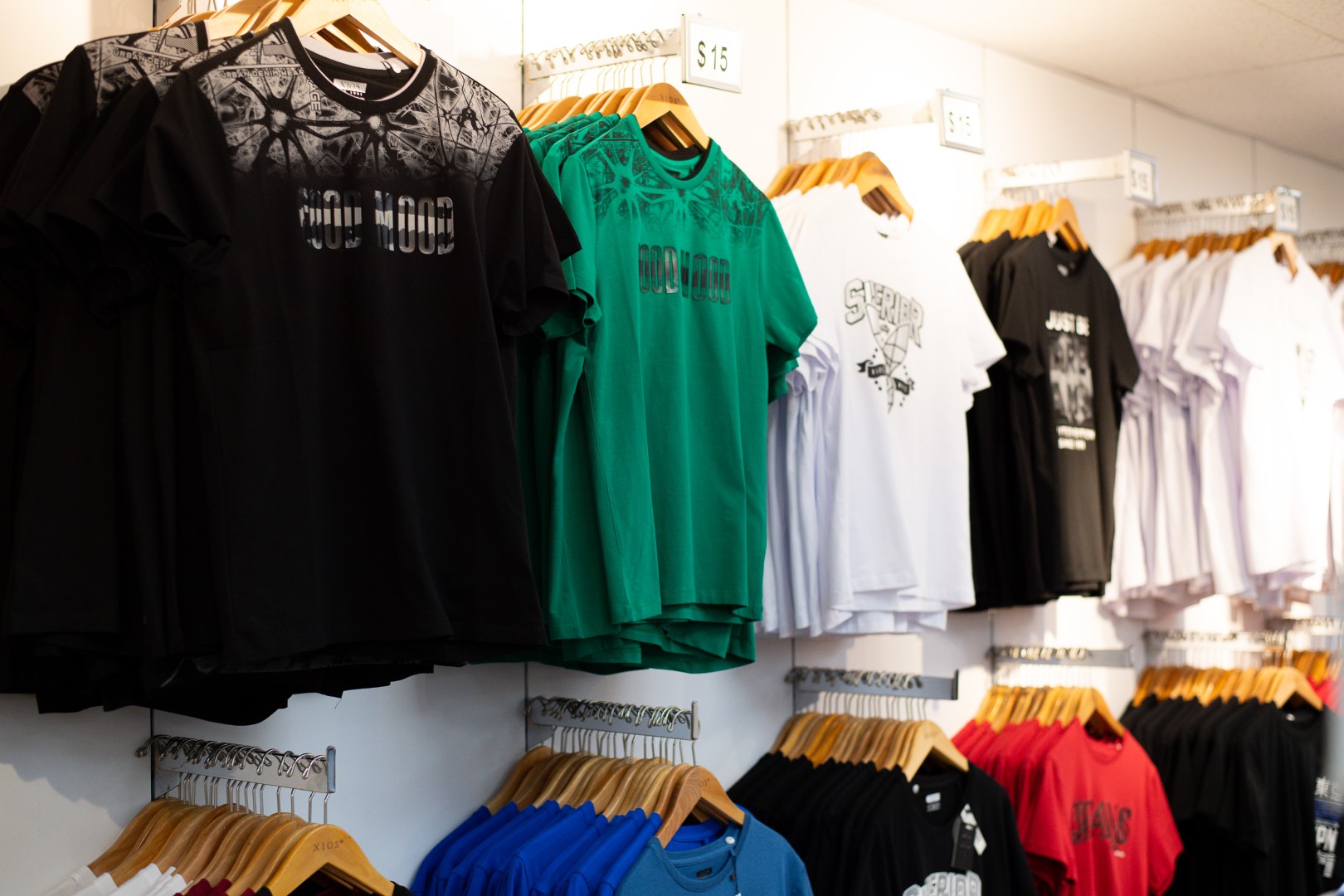 A variety of t-shirts displayed on wall-mounted racks in a store, featuring different colors and graphic designs, with price tags visible.