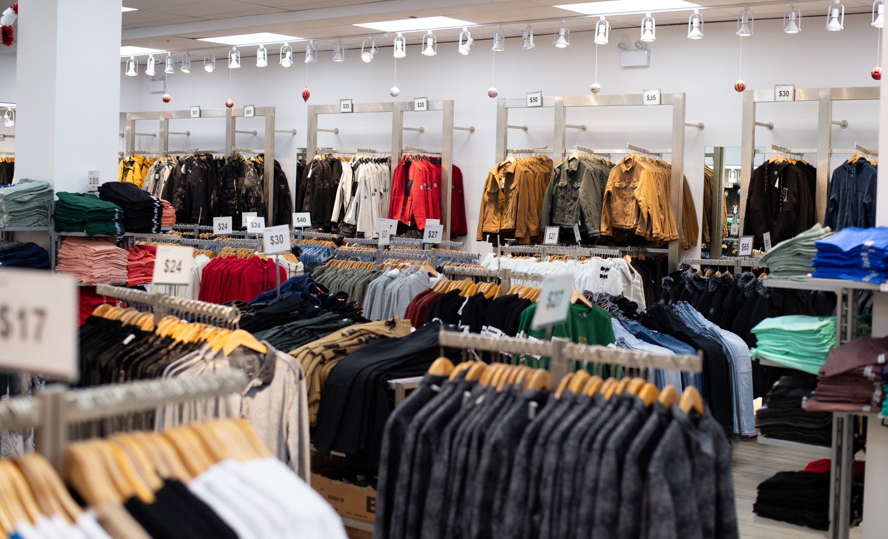 Interior of a clothing store with racks and shelves filled with various garments like jeans and jackets, prices displayed on signs, and soft lighting overhead.