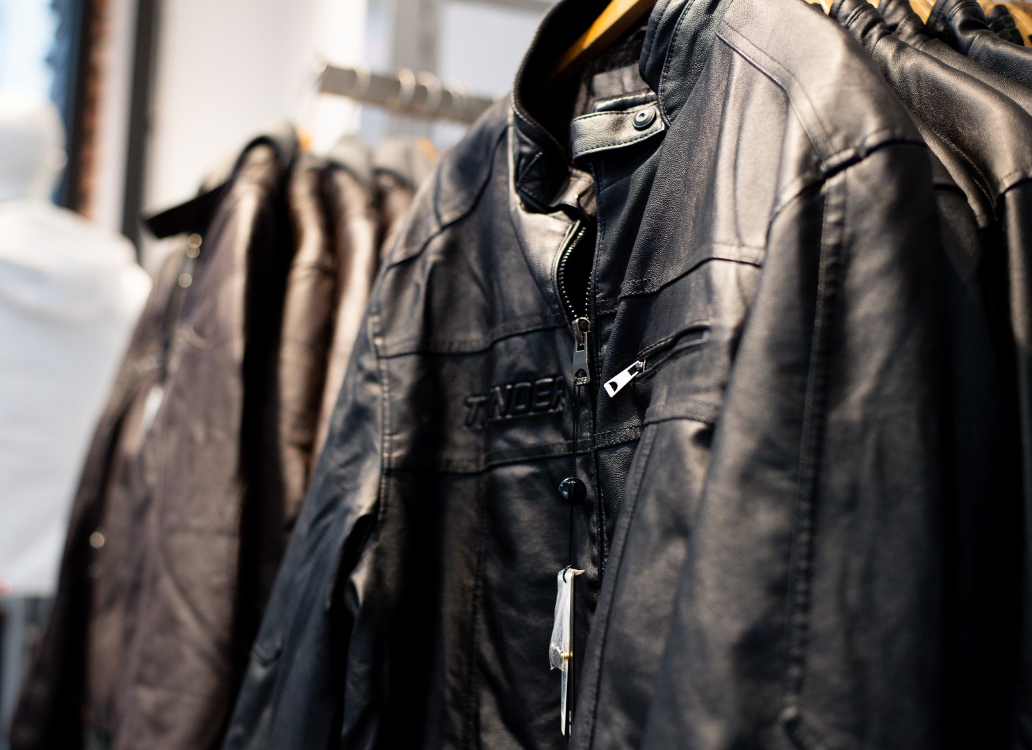Close-up of black leather jackets hanging on a rack in a clothing store, focused on intricate zipper details and textures.