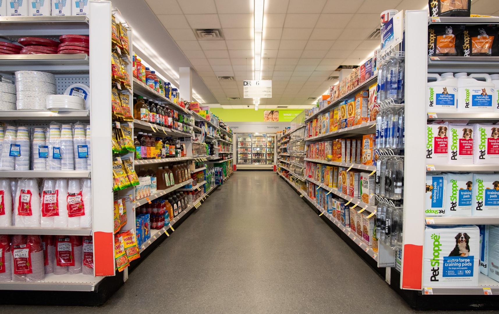 Interior of a supermarket showing aisles stocked with various packaged goods ranging from food items to household supplies, with clear aisle markers visible at the top.