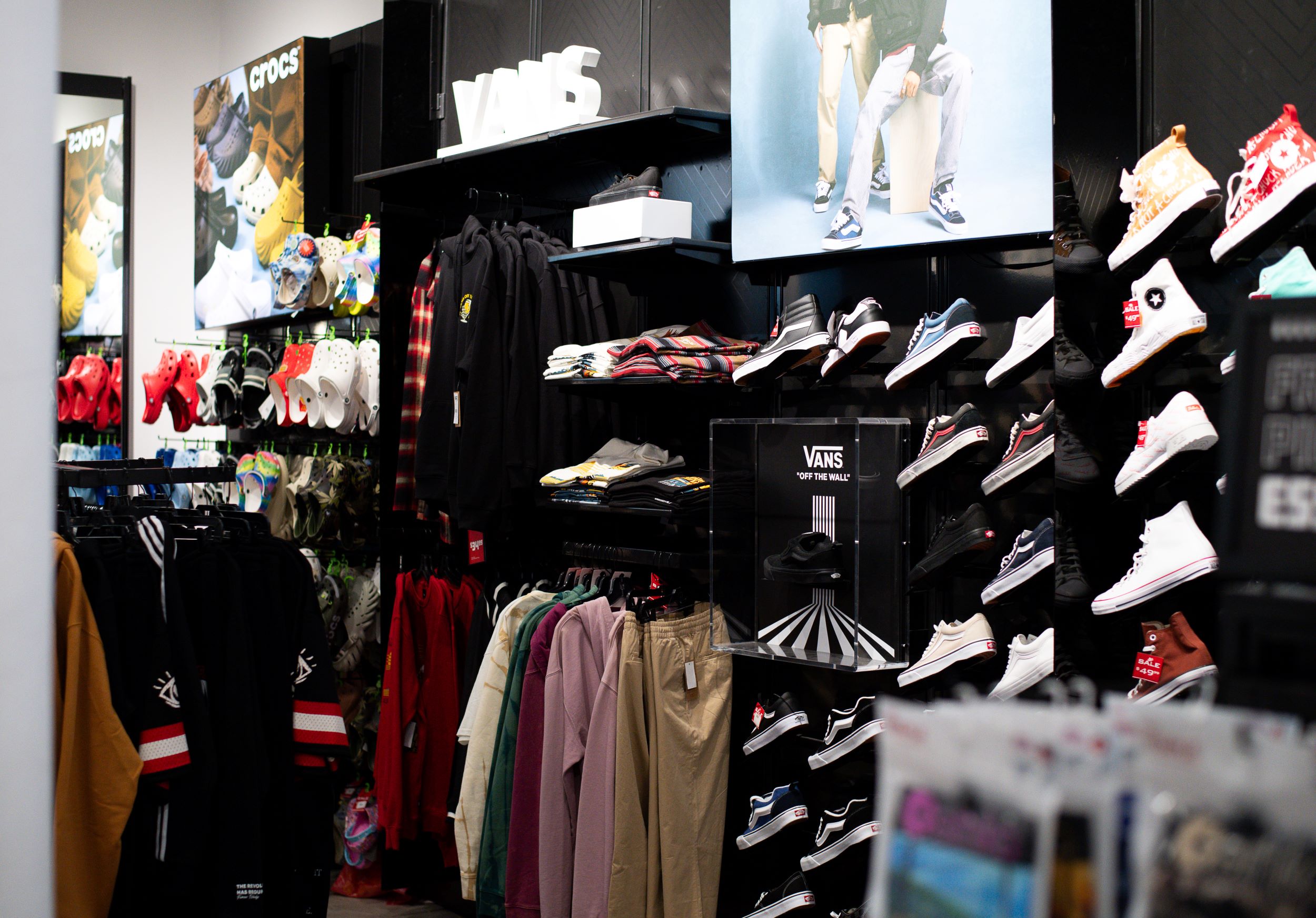 Interior of a clothing and shoe store with various branded merchandise like crocs and vans displayed on shelves and hanging racks. a colorful and organized space.