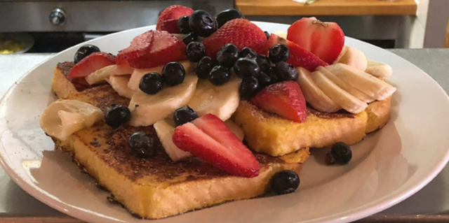 A plate of french toast topped with sliced bananas, strawberries, and blueberries, served on a kitchen counter.