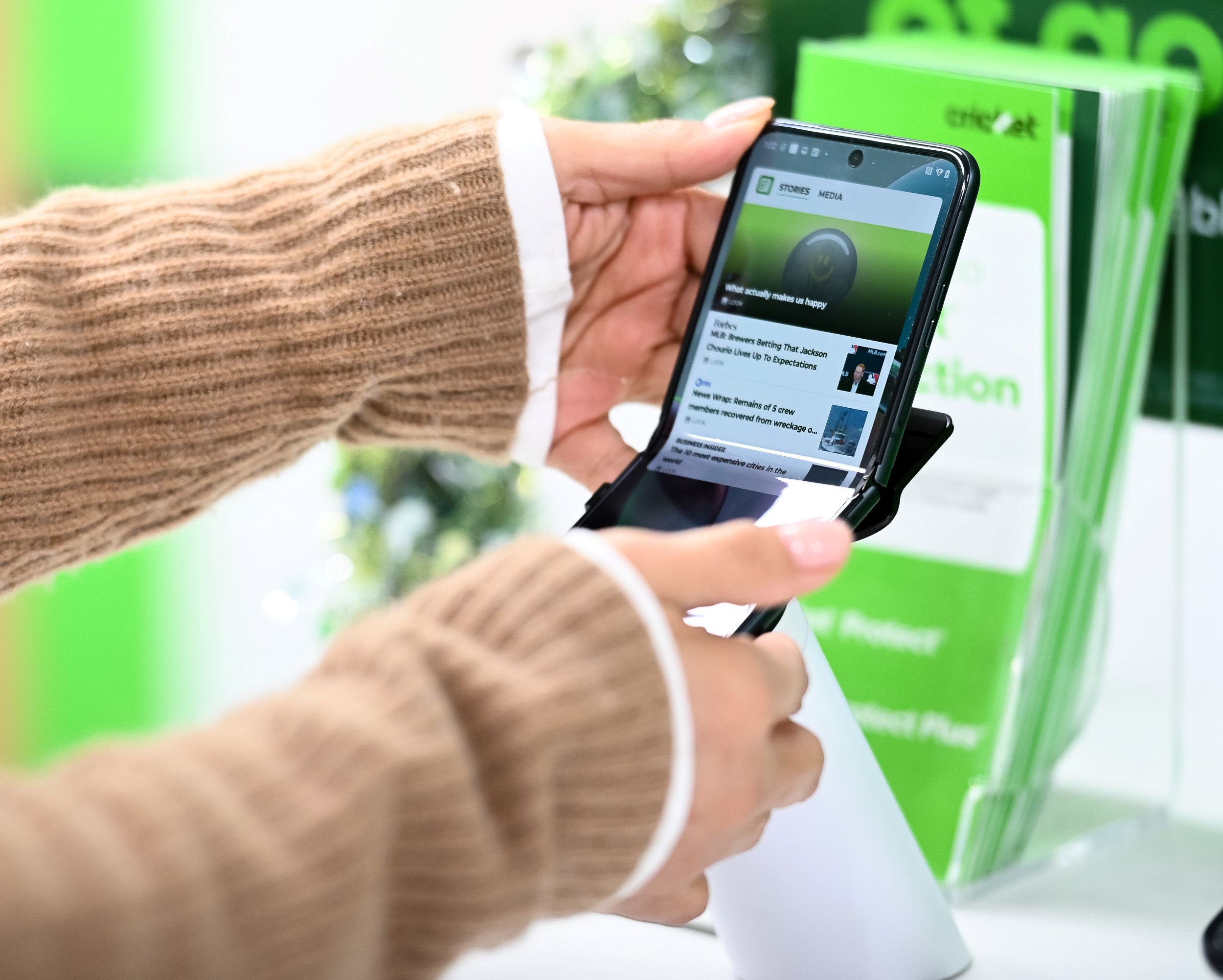 A person's hands holding a smartphone, displaying a webpage, over a green stand in a store with signage.