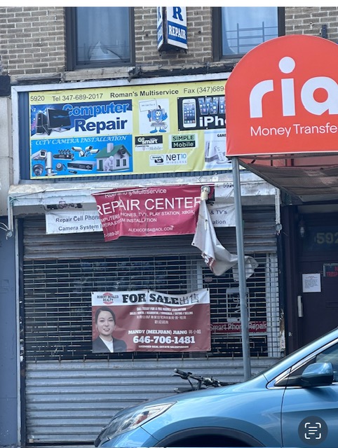 A storefront with various signs for different services, including computer repair, phone repair, and a money transfer service. One sign features a contact number for a "For Sale" listing. A blue car is parked in front of the shuttered entrance.