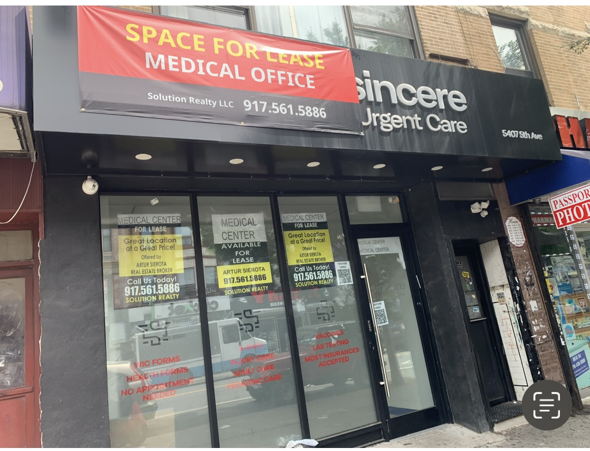 Storefront with a sign on top reading "SPACE FOR LEASE MEDICAL OFFICE" by Solution Realty LLC with a contact number. Next to it is a sign for "Sincere Urgent Care" and a neighboring "Passport Photos & Notary" sign. The doors display more leasing details.